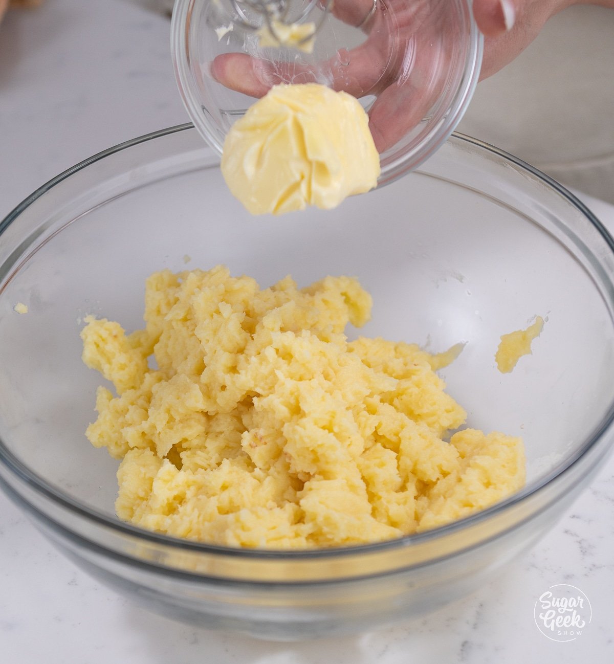 hand adding butter to pastry cream mixture in a bowl.