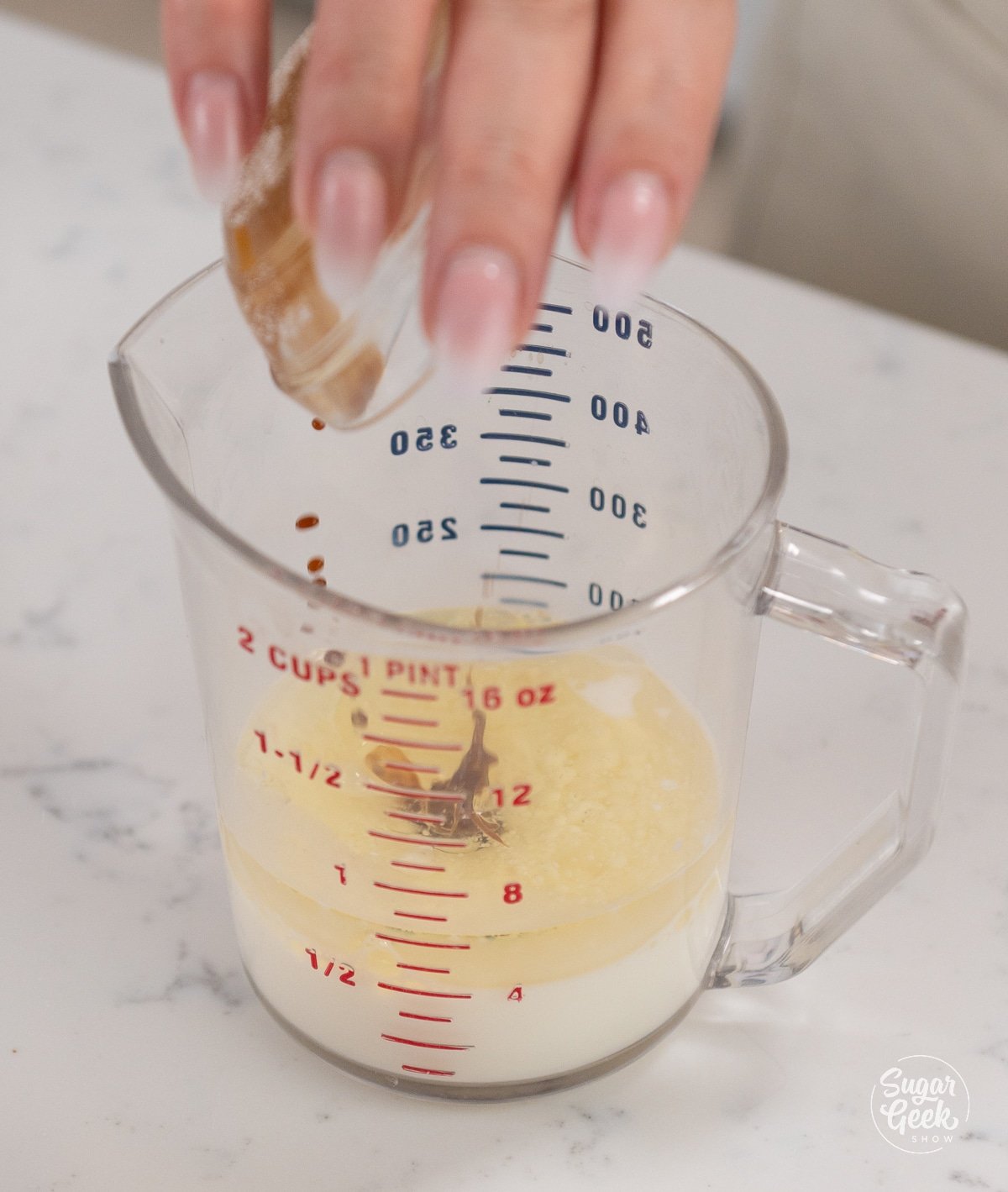 hand adding vanilla to milk and oil mixture in a measuring cup. 