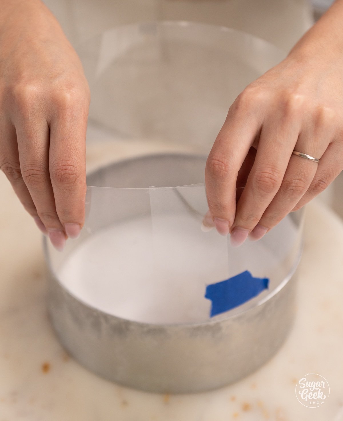 hands placing an acetate sheet into a cake ring.