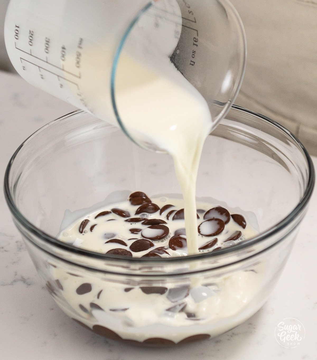 hands pouring cream over chocolate in a bowl.