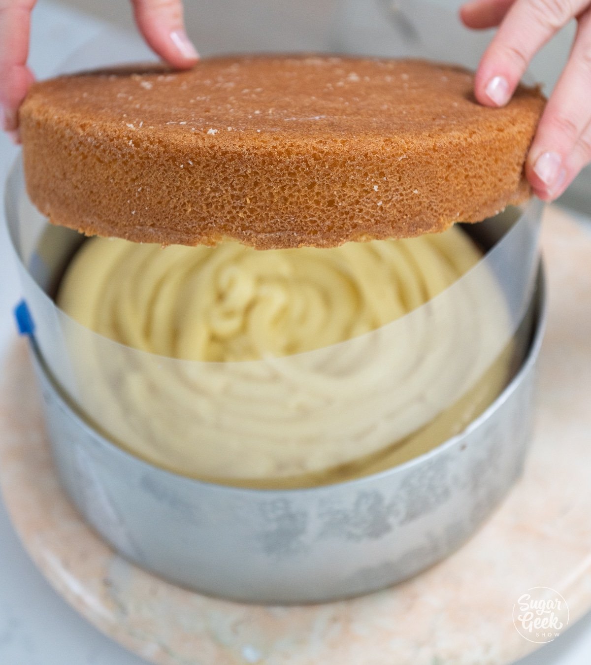 hands adding second cake layer on top of pastry cream filling.