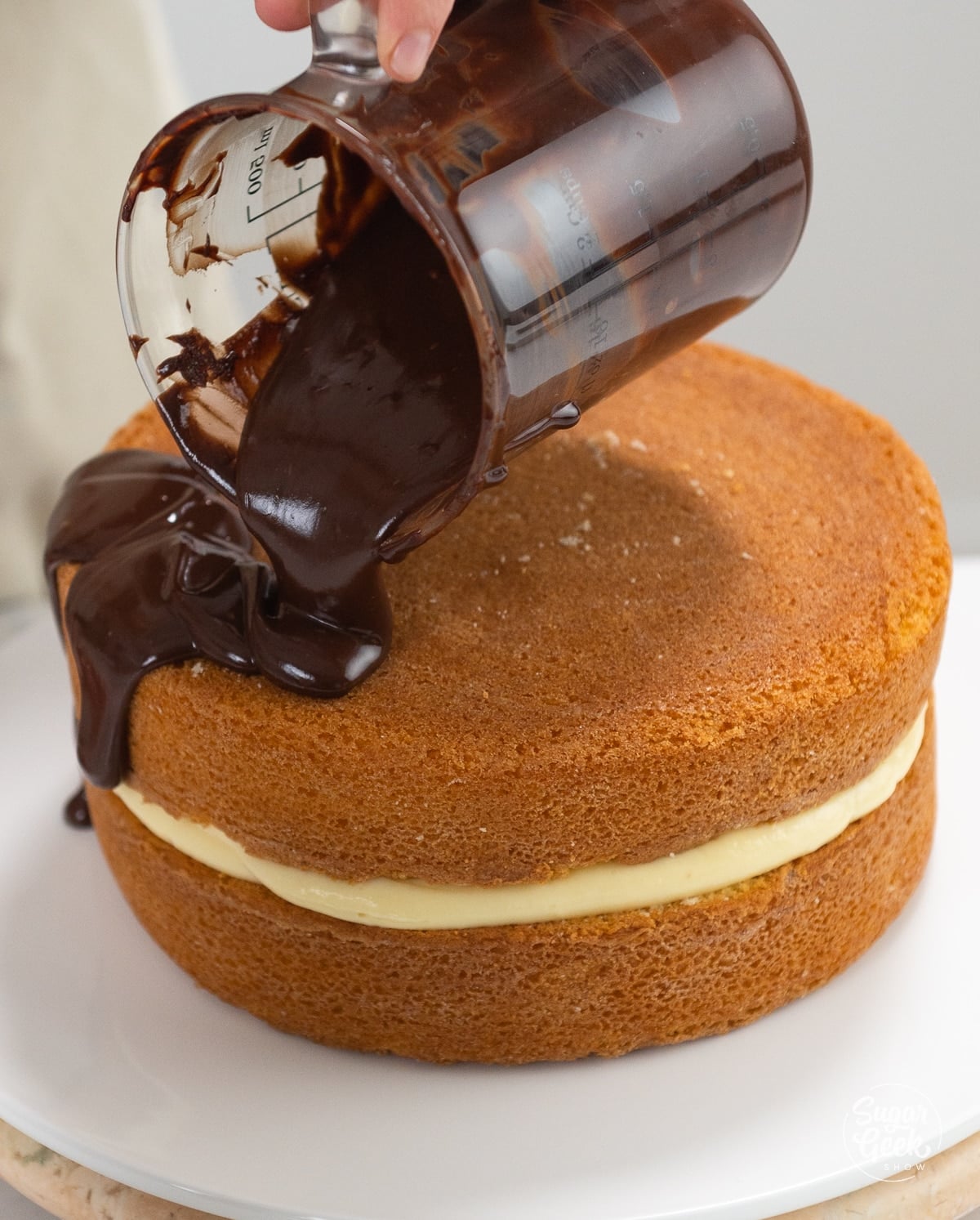 hand pouring ganache on top of filled cake layers.