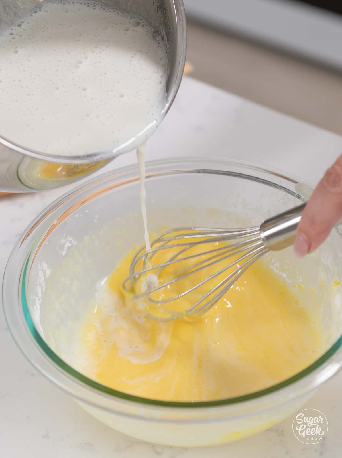 hand slowly pouring warm milk mixture into egg mixture while whisking.  