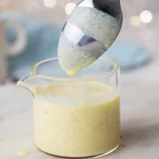 close up of spoon dipped in creme anglaise in a clear container