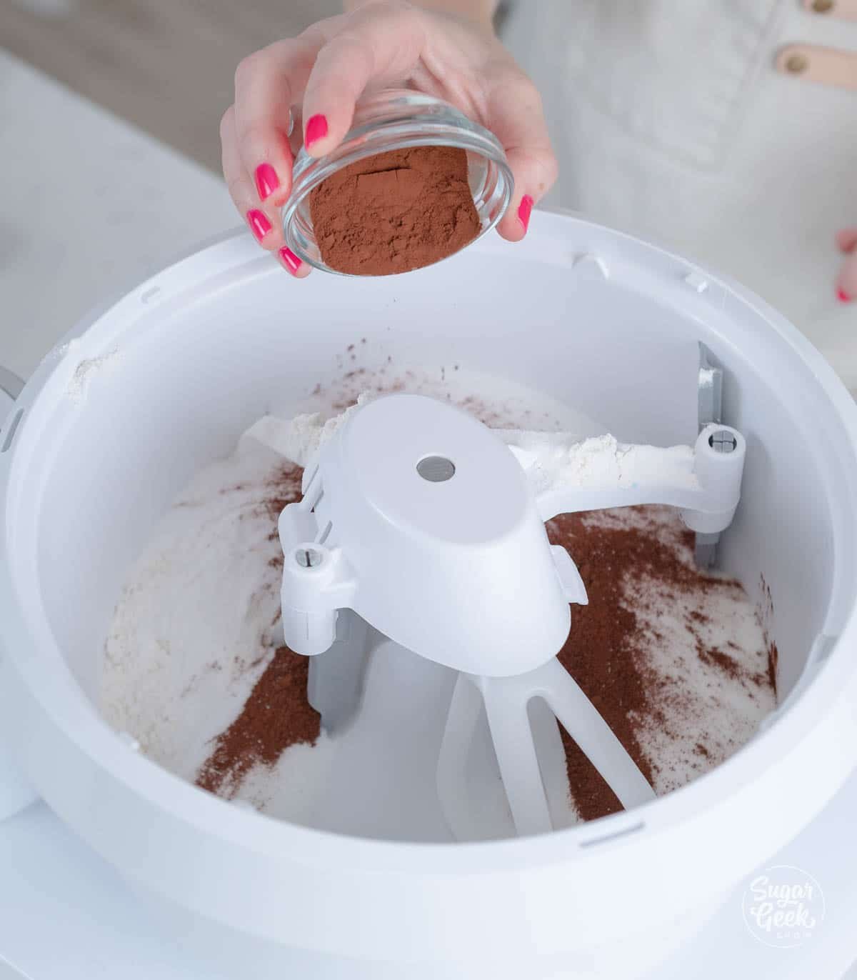 hand adding cocoa powder to mixing bowl with dry ingredients.
