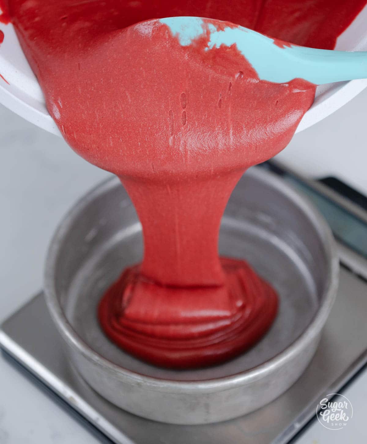 Pouring finished red velvet cake batter into a cake pan.