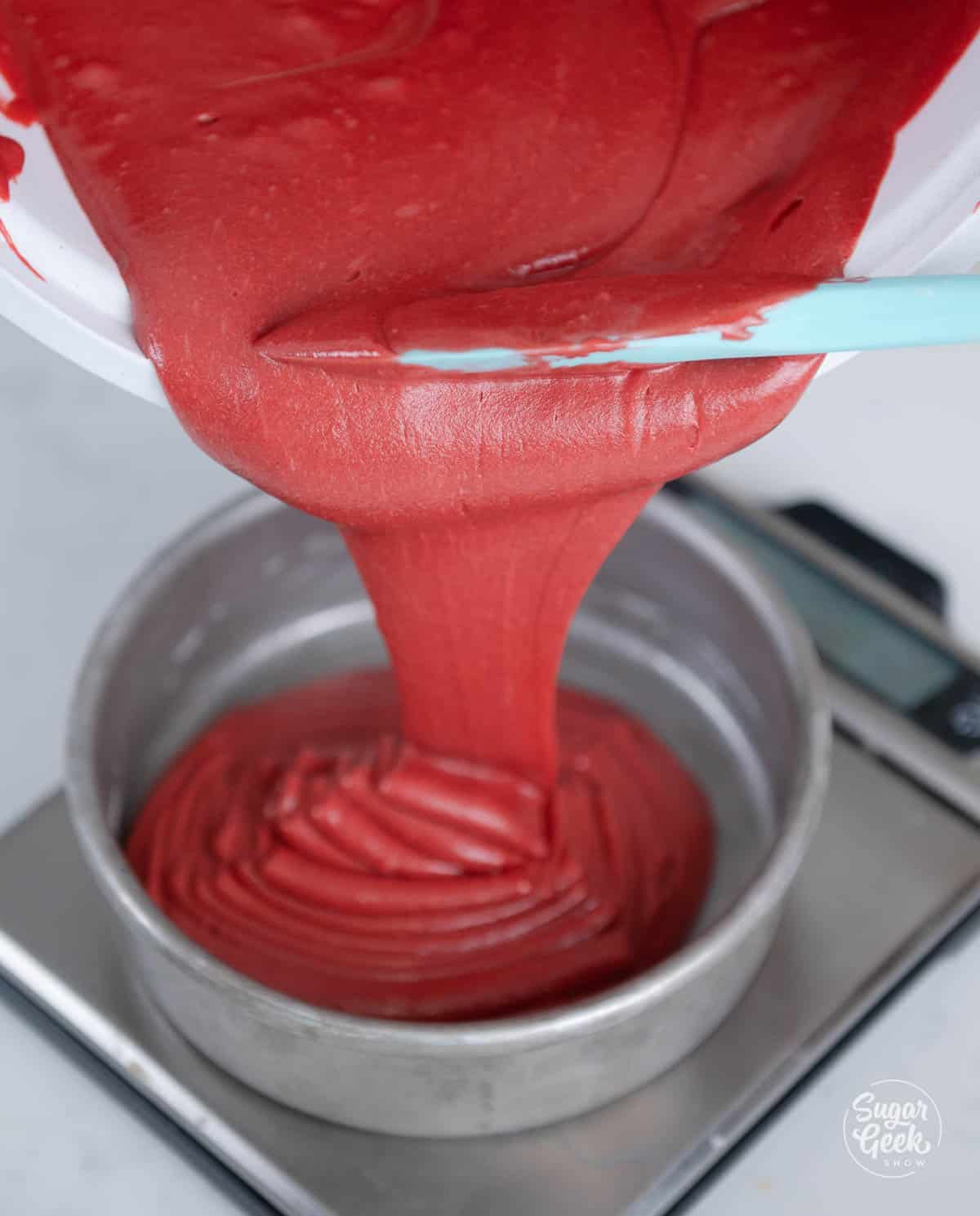 Pouring finished red velvet cake batter into a cake pan.