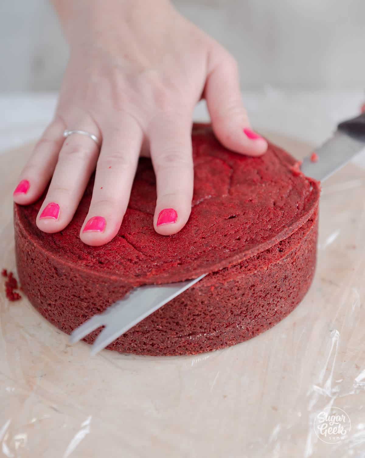 hands trimming domed top off of a layer of cake with a serrated knife.