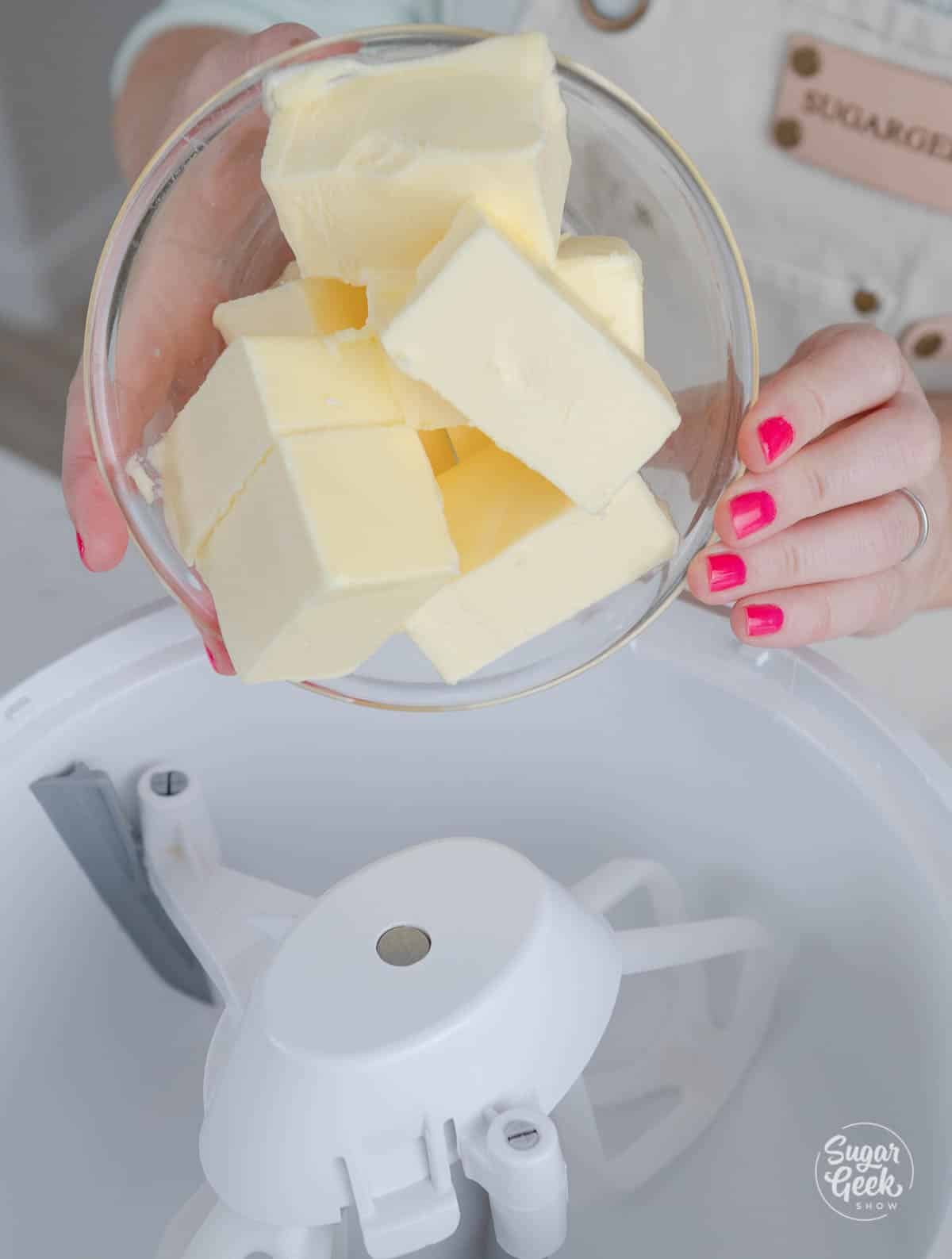 hands putting butter into stand mixer bowl.