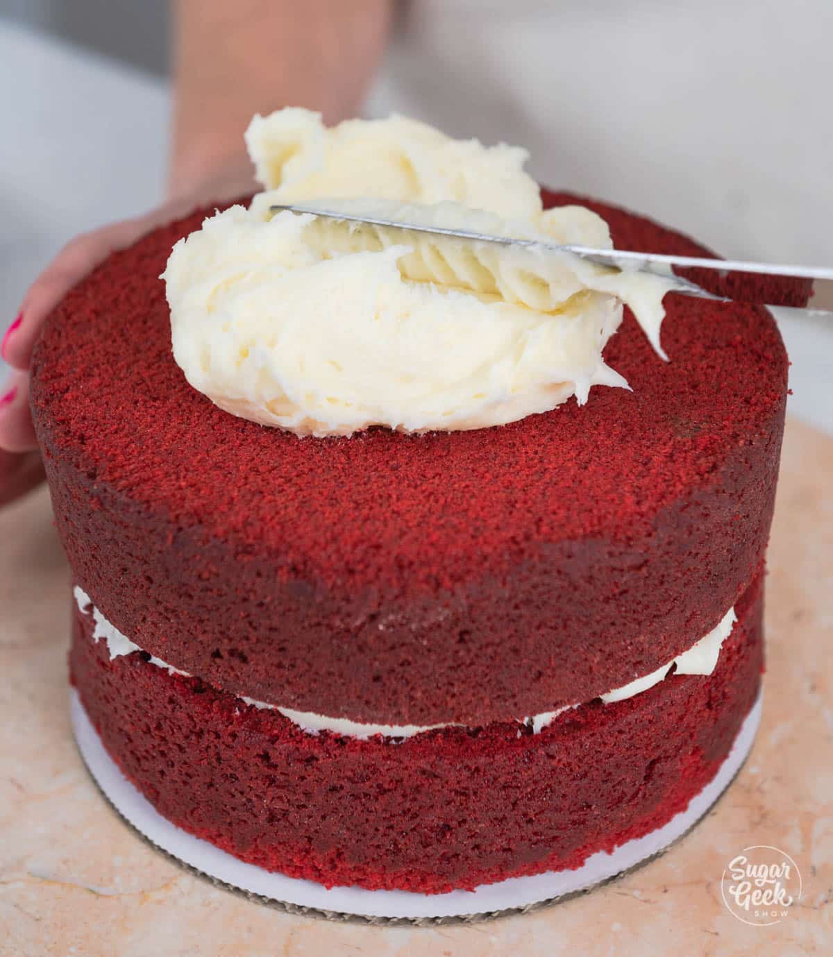 hands spreading cream cheese frosting on second layer of cake with a spatula. 