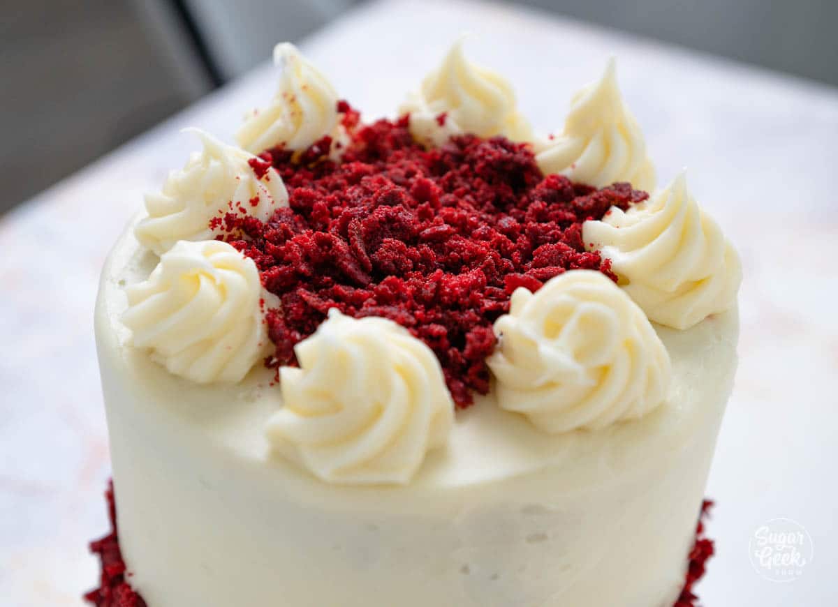 Top of a cake with cream cheese dollops and red velvet crumbles in the middle.
