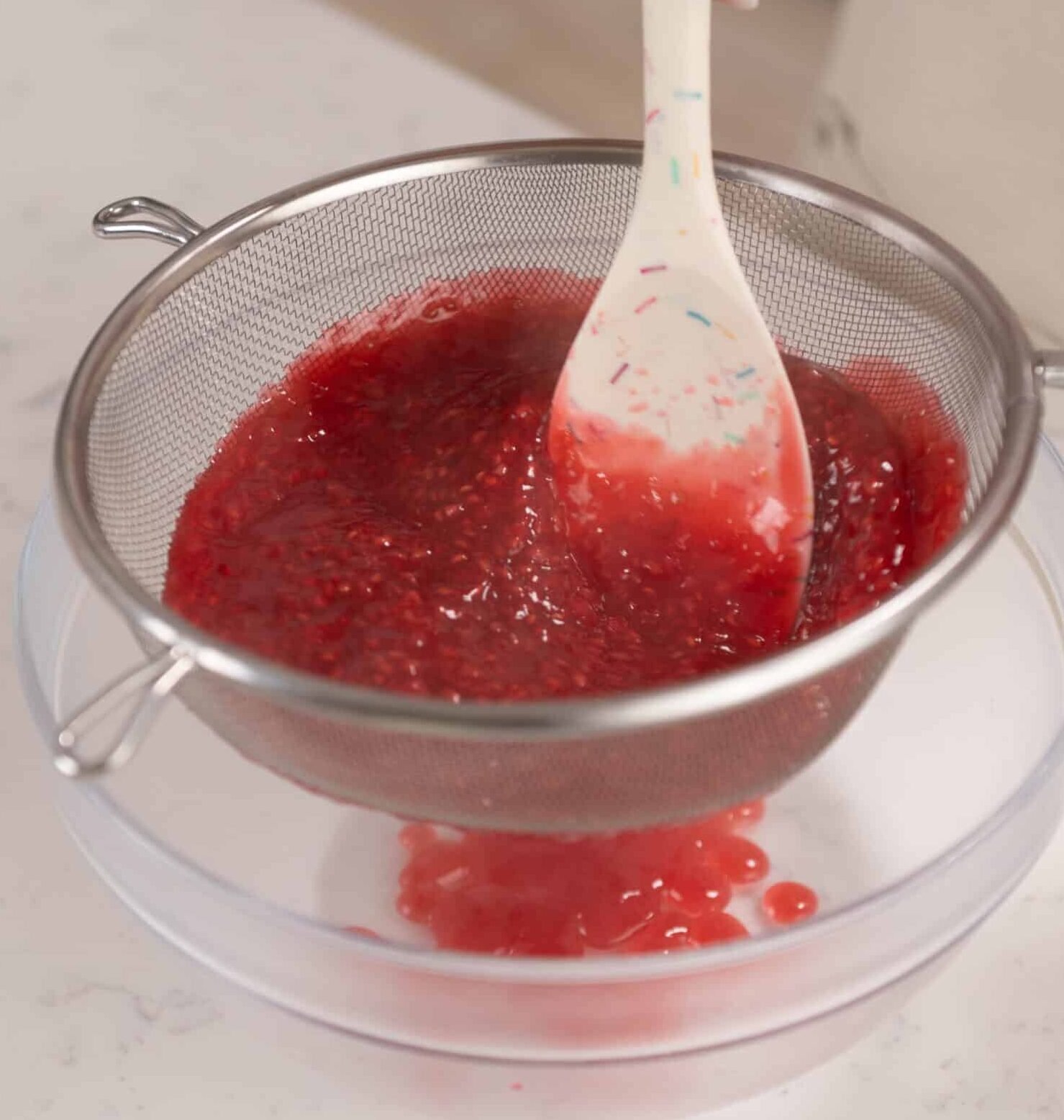 raspberry filling being strained into a bowl to remove the seeds