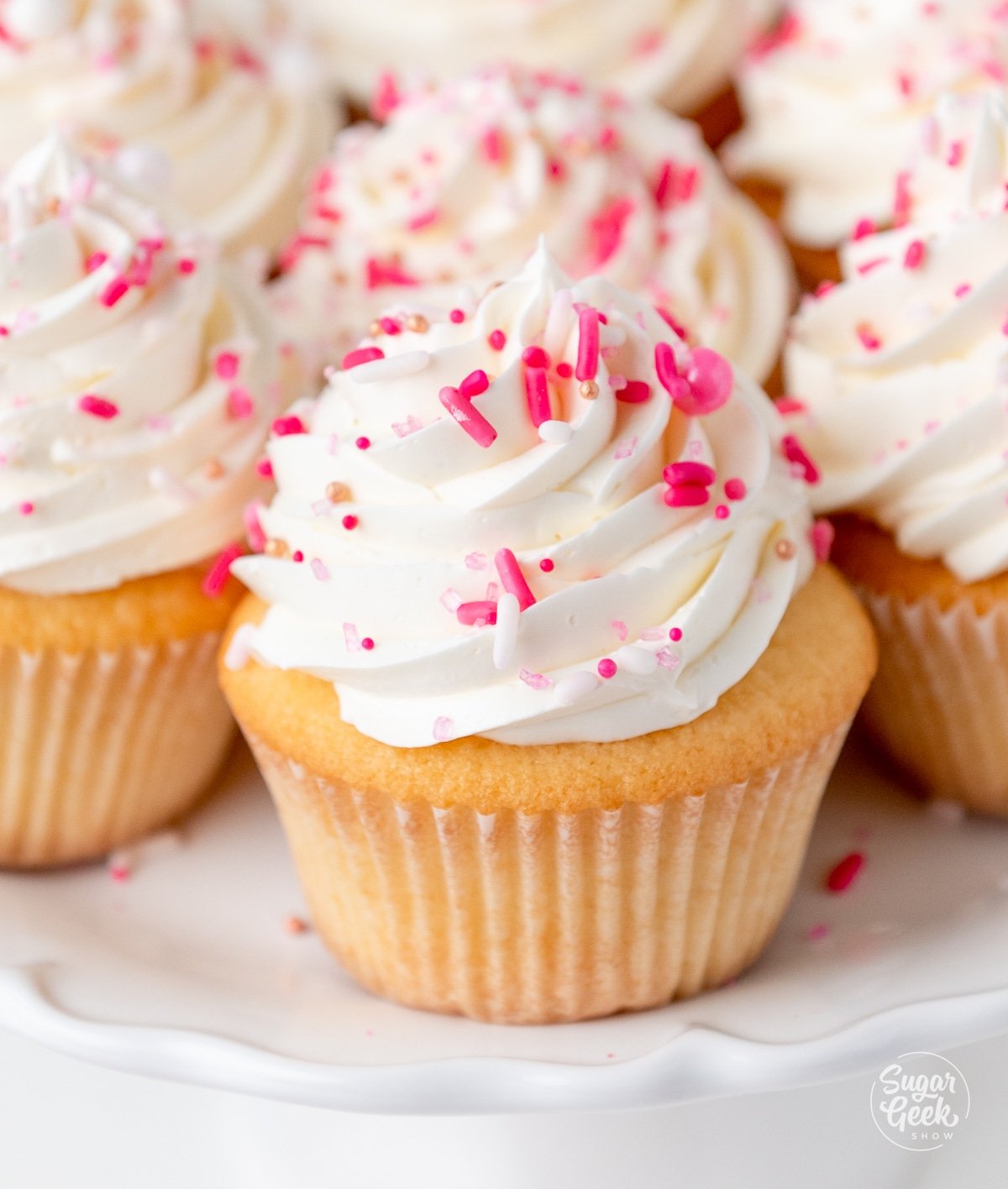 plate of finished vanilla cupcakes with pink sprinkles.