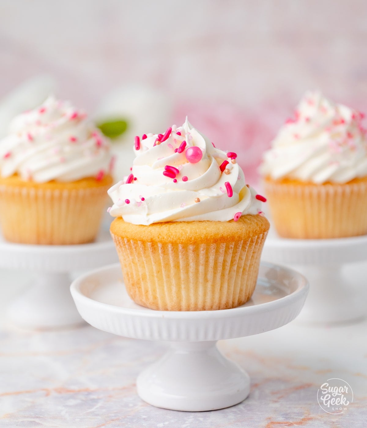 A moist vanilla cupcake on a white stand with more in the background. 