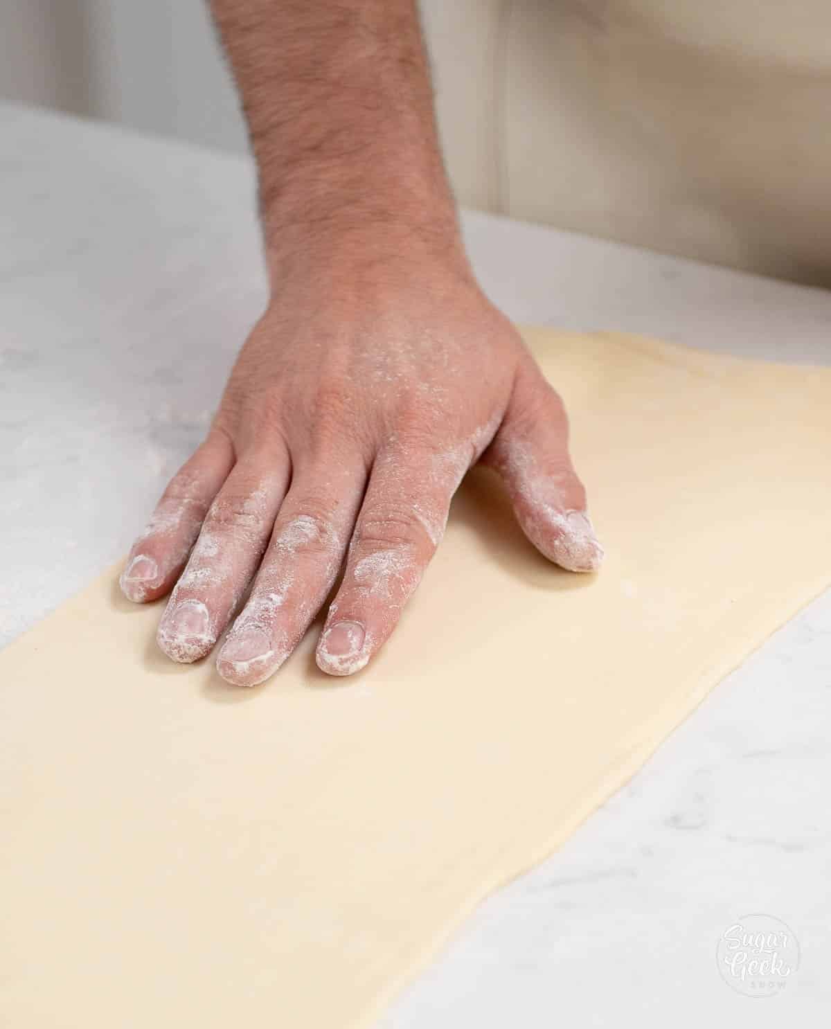 hand dusting sheet of rolled dough with flour