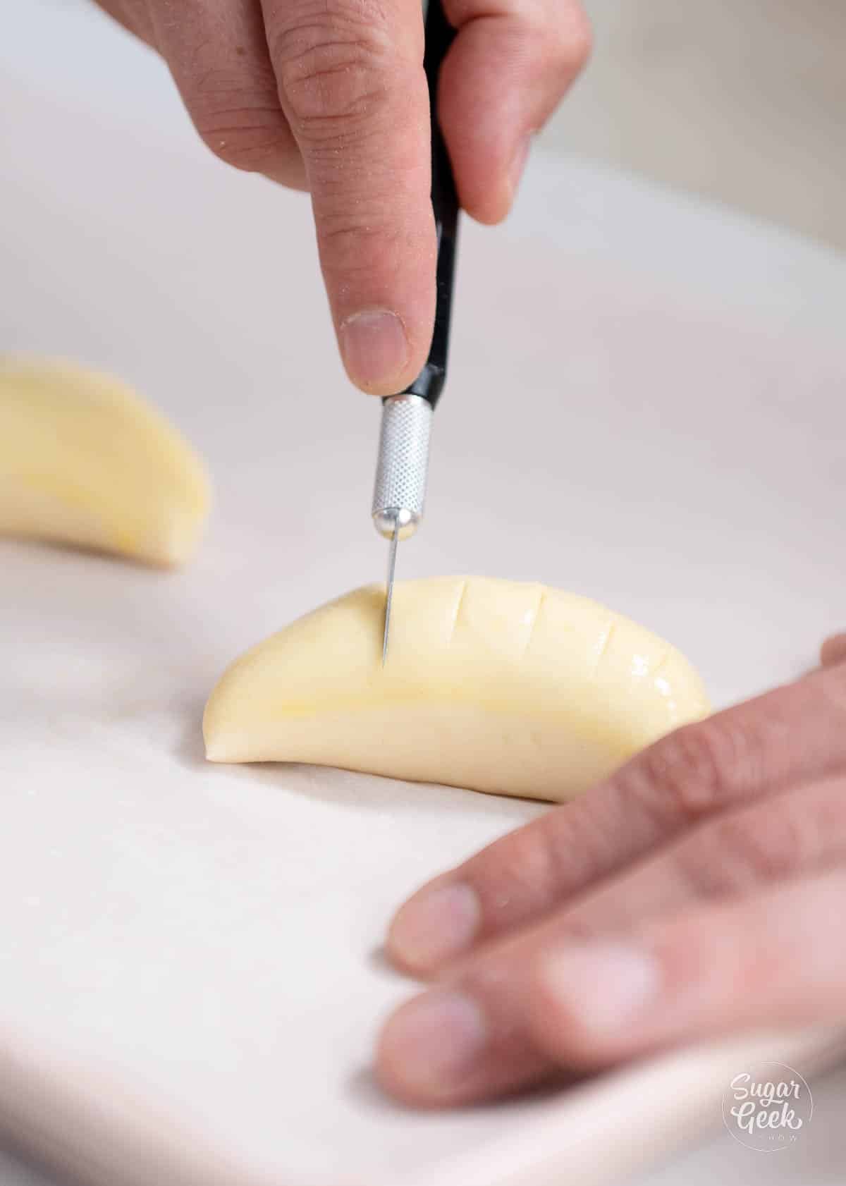 Hand using an exacto knife to cut a shell pattern on top of the turnover. 