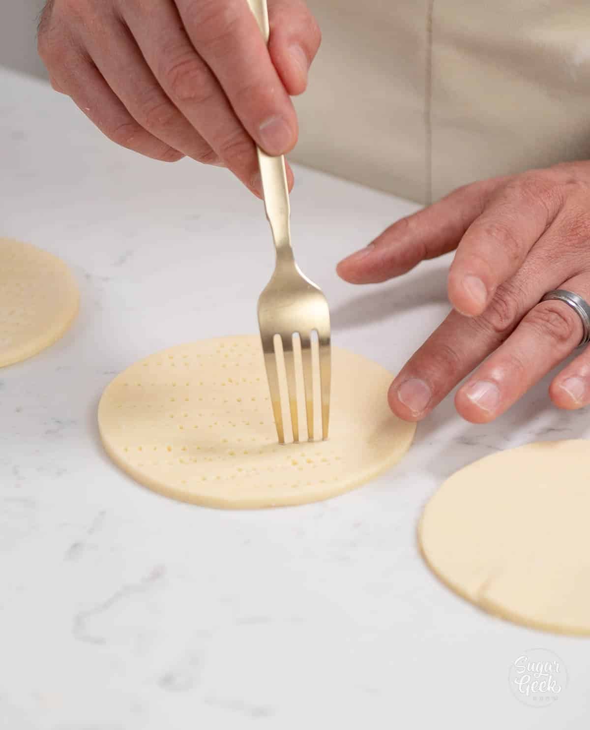 hand using a fork to dock the dough circles. 
