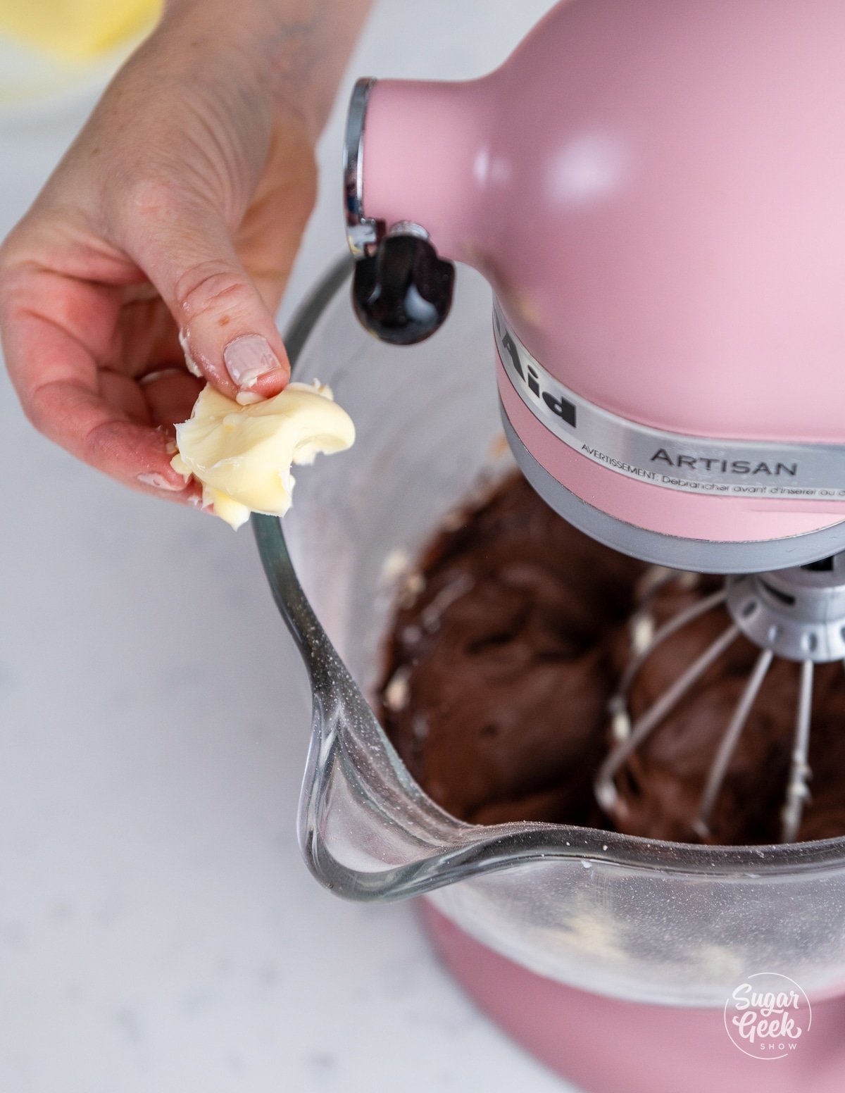 hand adding chunks of softened butter to the stand mixer.