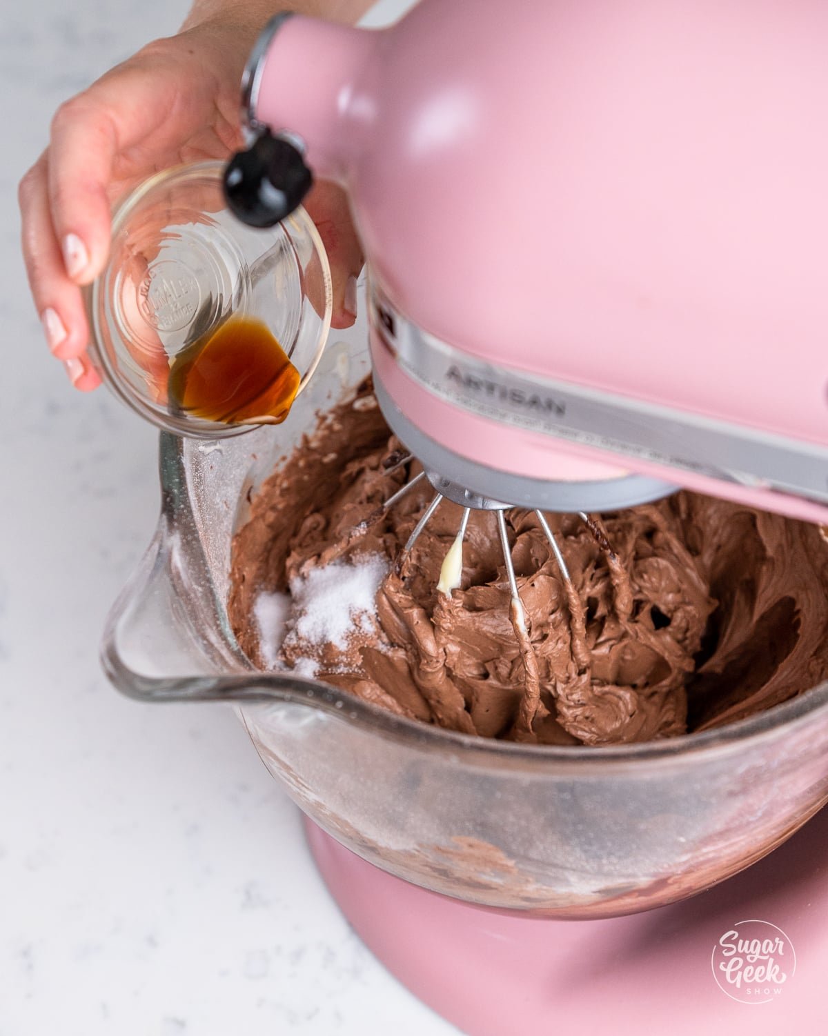 hand adding vanilla to the stand mixer.
