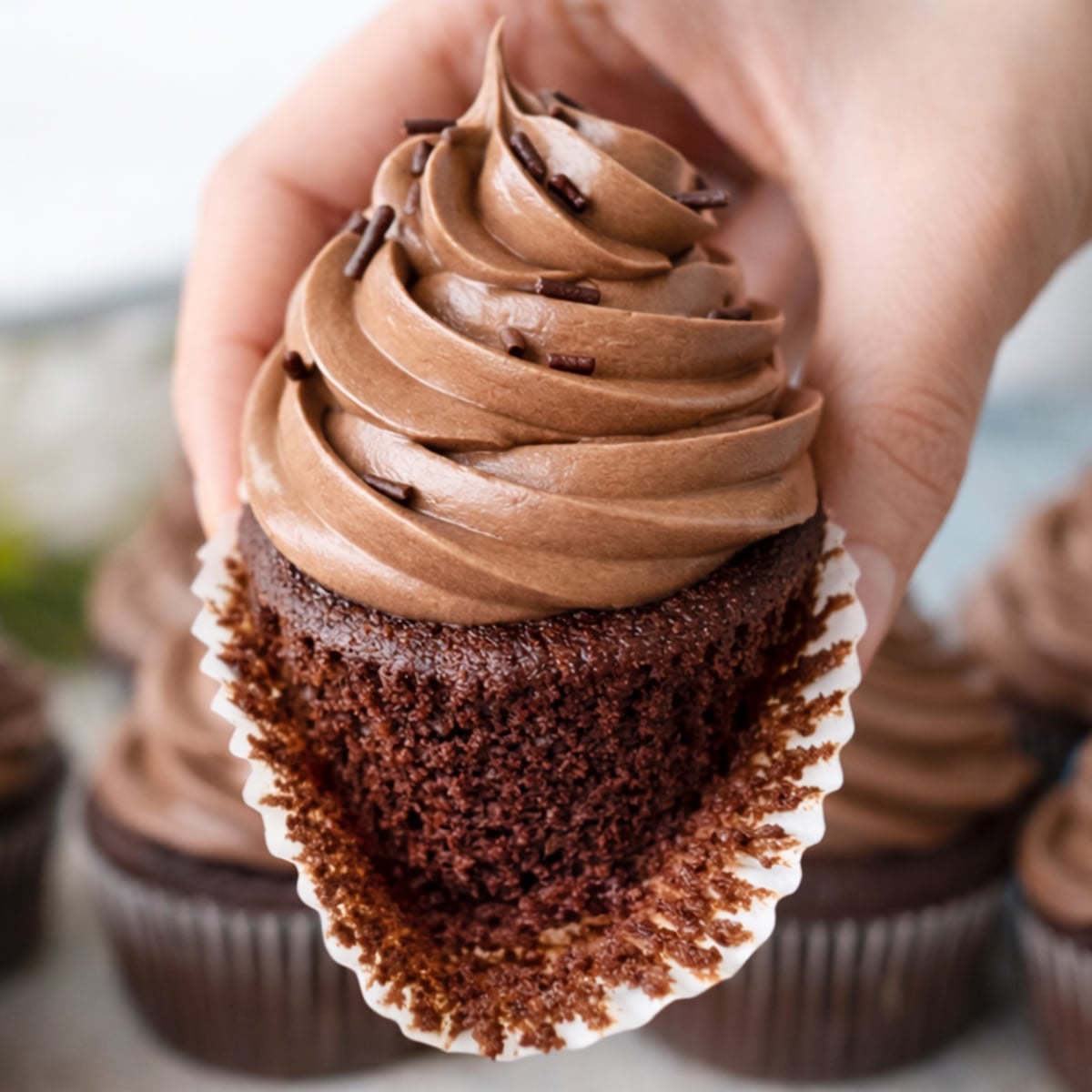 Chocolate cupcake recipe with moist chocolate cake and smooth chocolate buttercream frosting, liner peeled back to show soft crumb