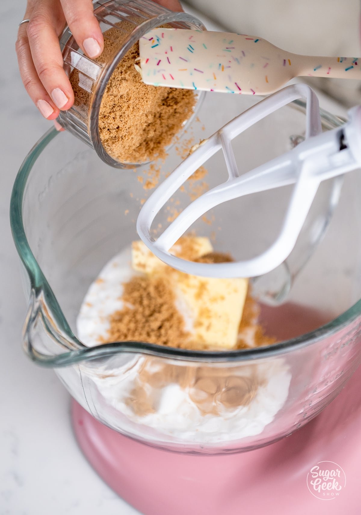 hand adding brown sugar to stand mixer bowl with butter and sugar.