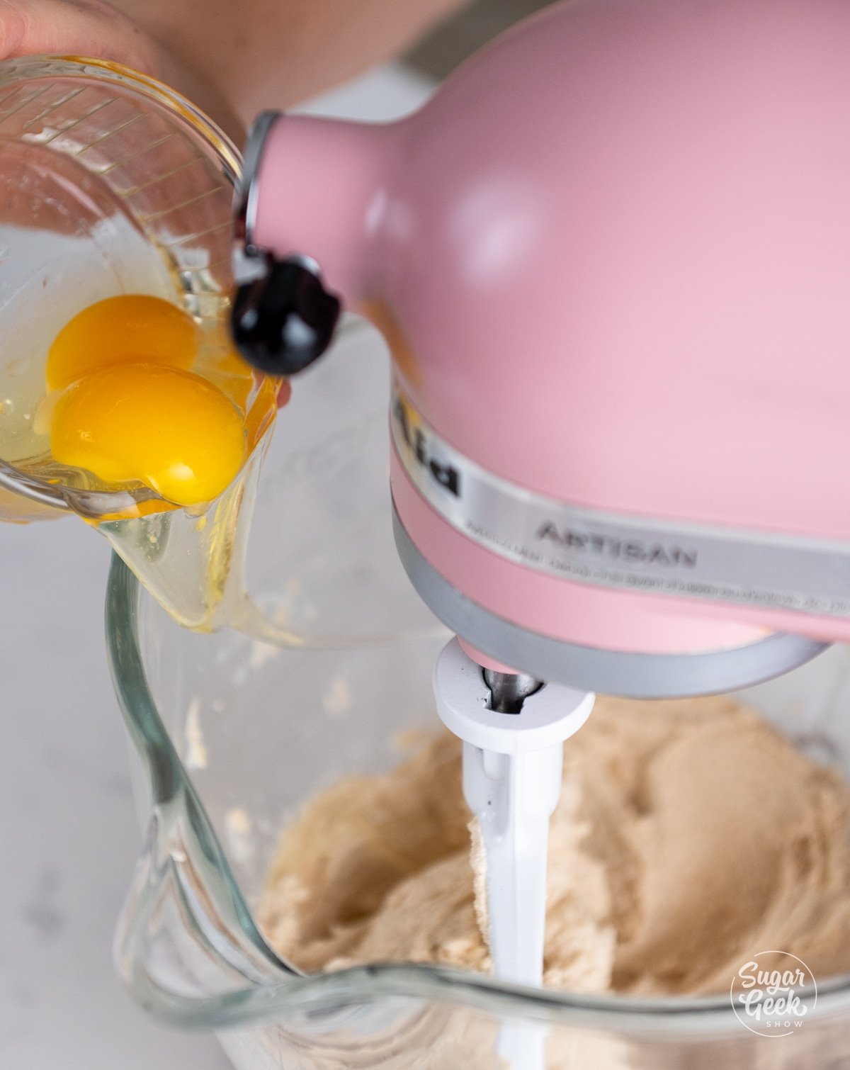 hand adding eggs one at a time to to the stand mixer.