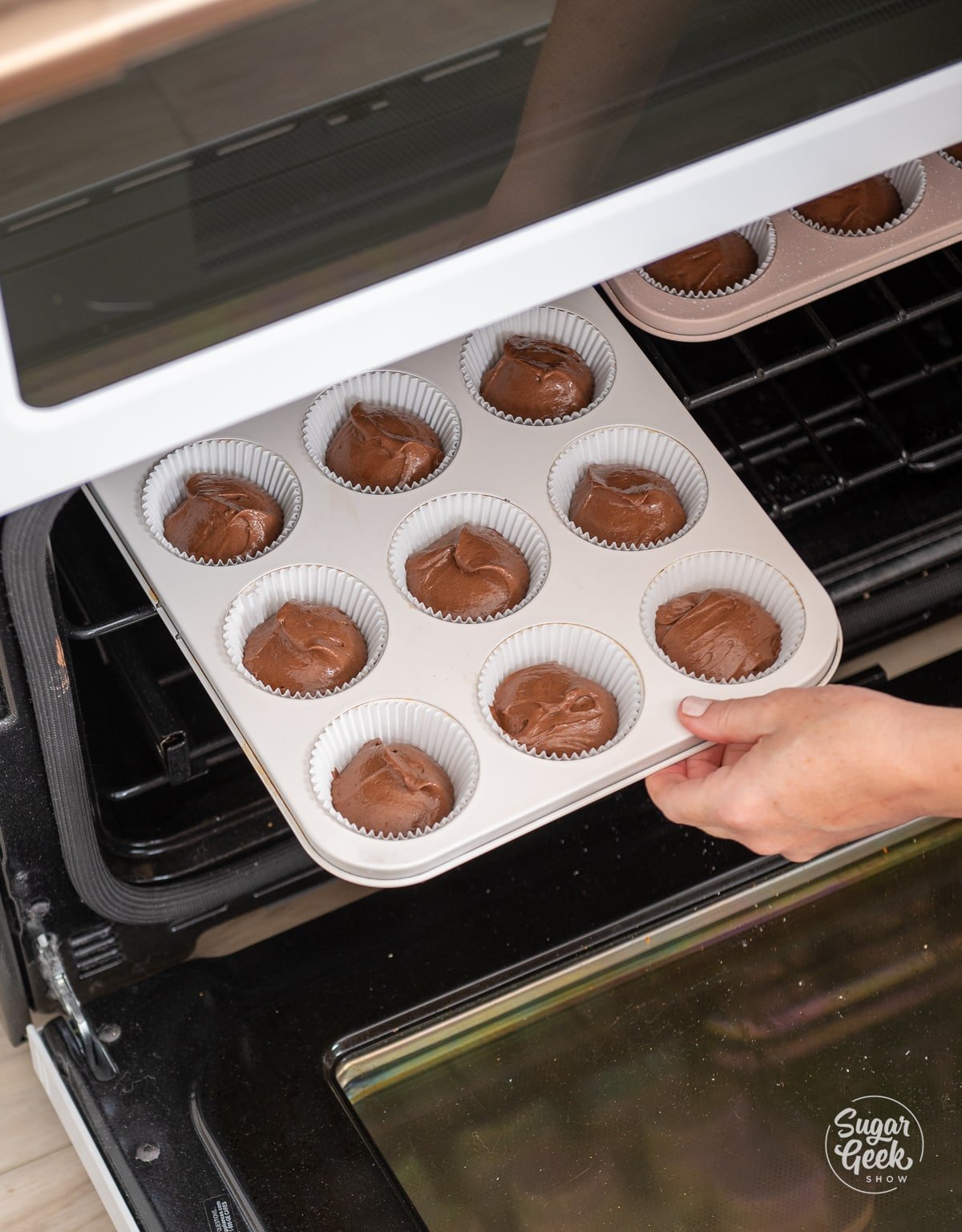 hand placing cupcake pans into oven.