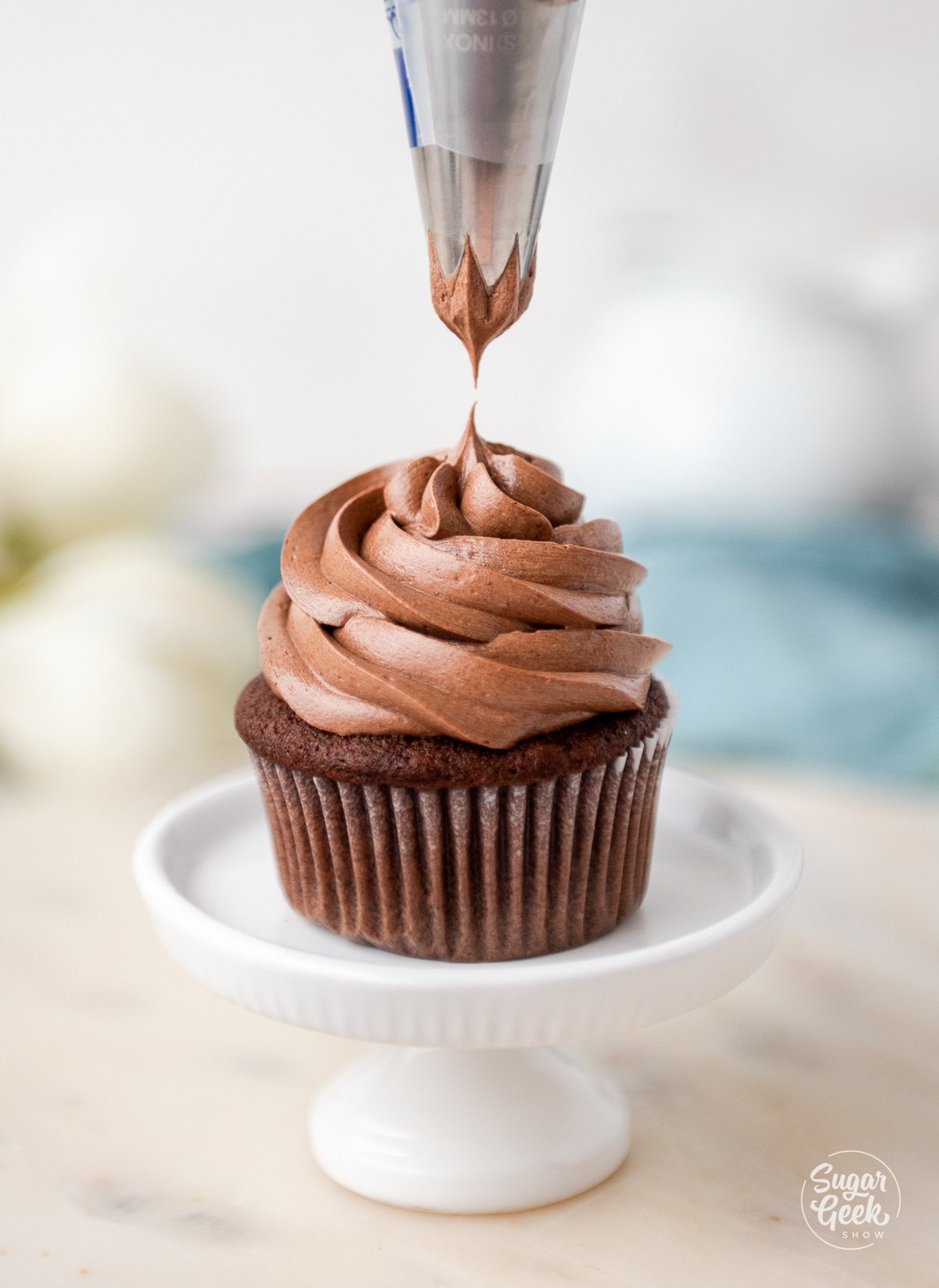 piping frosting onto a chocolate cupcake.