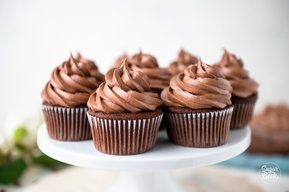 close up of finished chocolate cupcakes with chocolate buttercream frosting on a white plate