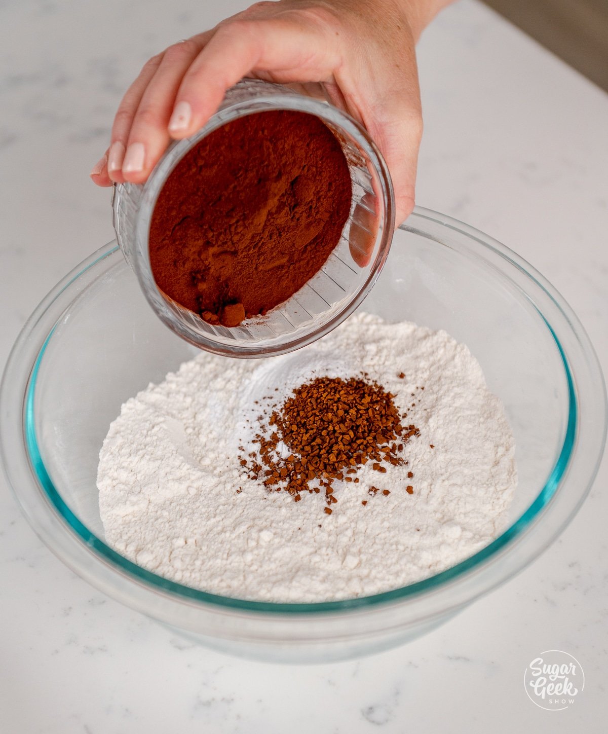 hand adding cocoa powder to other dry ingredients in a bowl. 