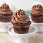 Moist chocolate cupcake with chocolate buttercream frosting on a white cake stand