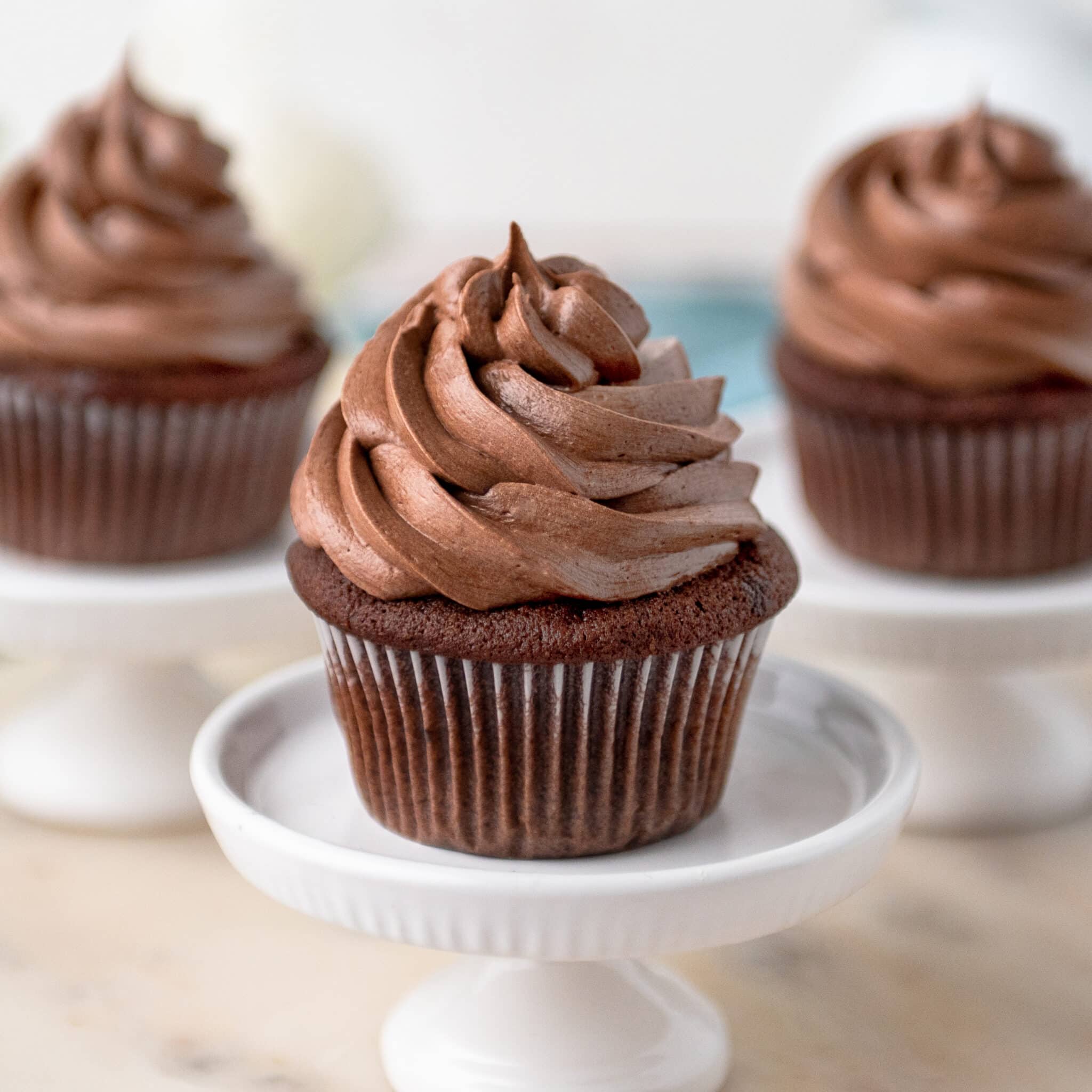 Moist chocolate cupcake with chocolate buttercream frosting on a white cake stand