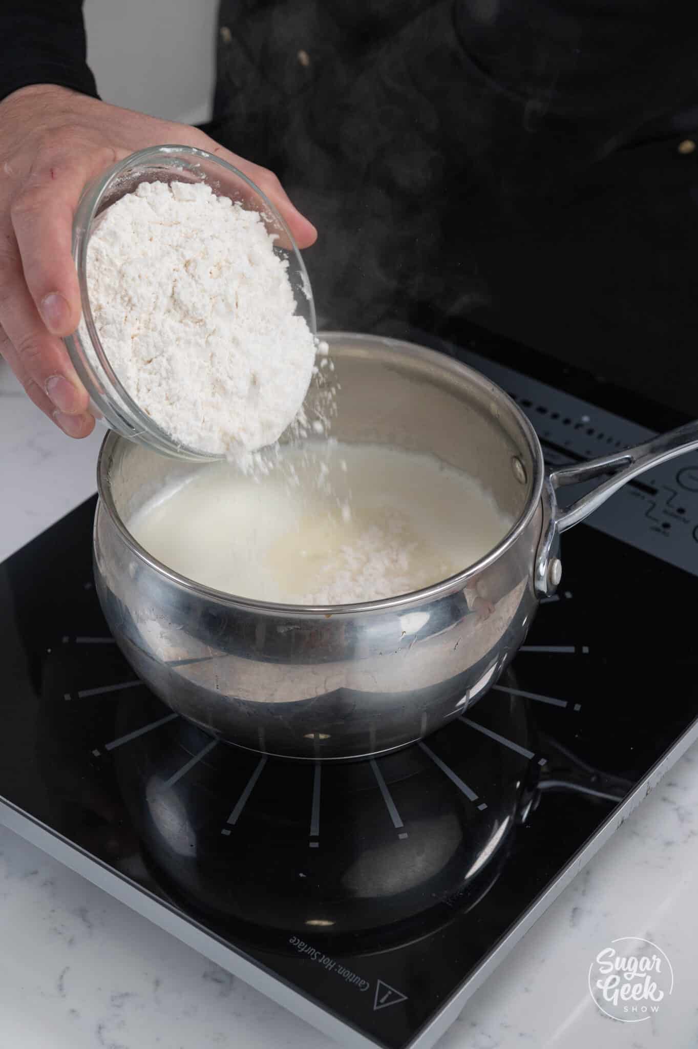 flour pouring into a pot of milk over the stove