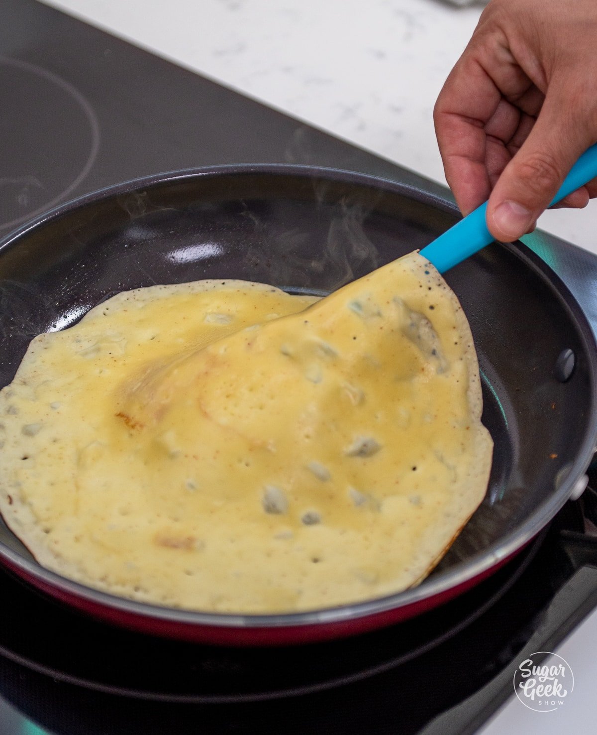 spatula underneath a crepe on a pan ready to be flipped