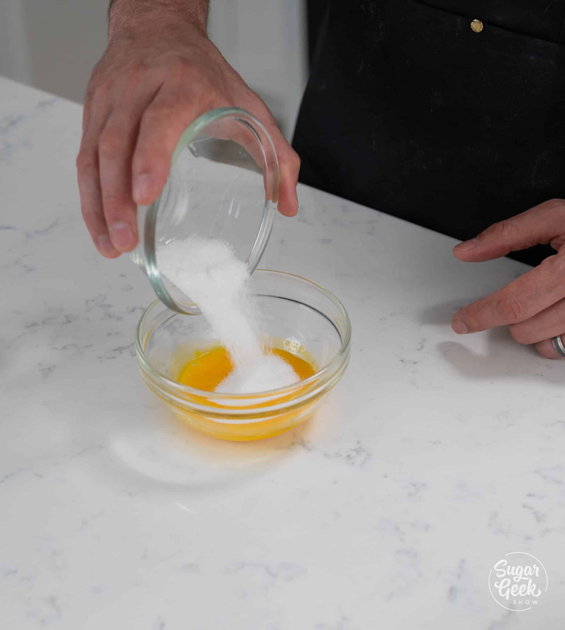pouring sugar into a bowl of egg yolks