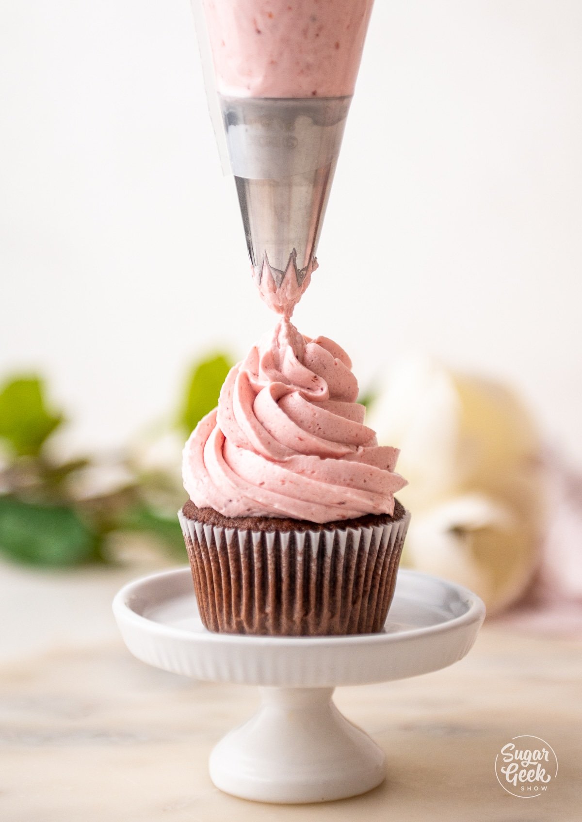 piping bag piping a swirl of strawberry buttercream on top of a chocolate cupcake