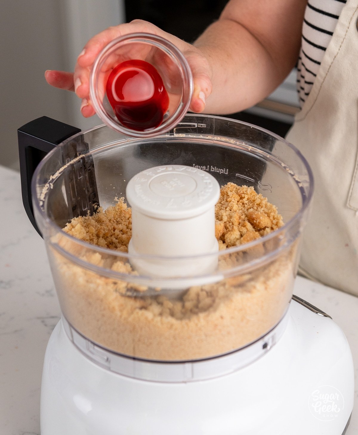 hand adding strawberry emulsion to the food processor.