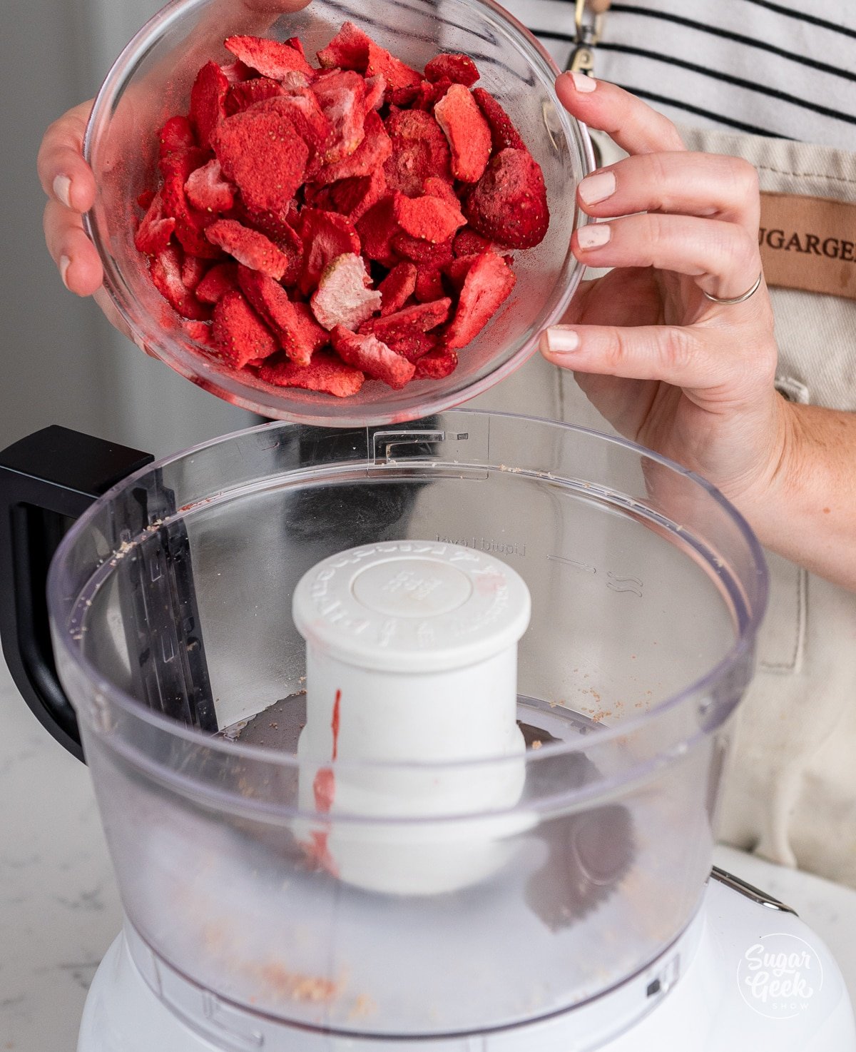 hands pouring freeze dried strawberries into a food processor.