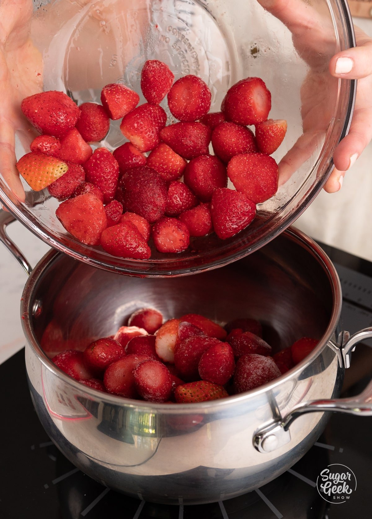 hands adding frozen strawberries to a pot.