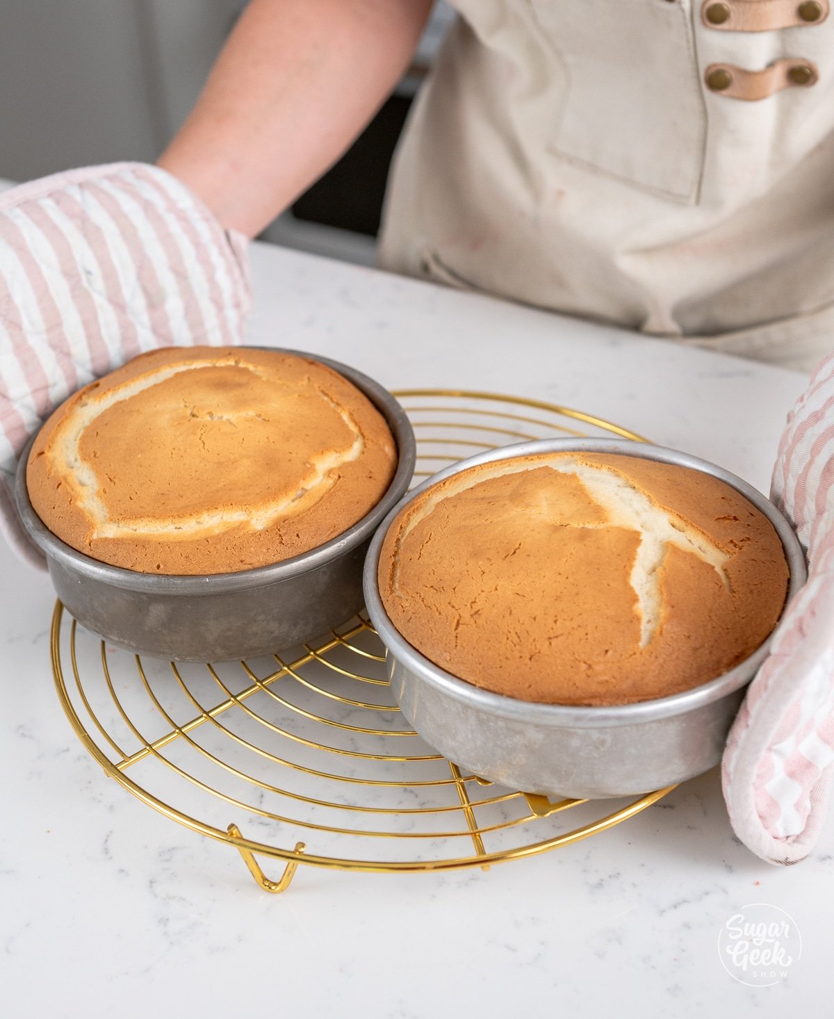 hands placing baked white cakes on a cooling rack. 