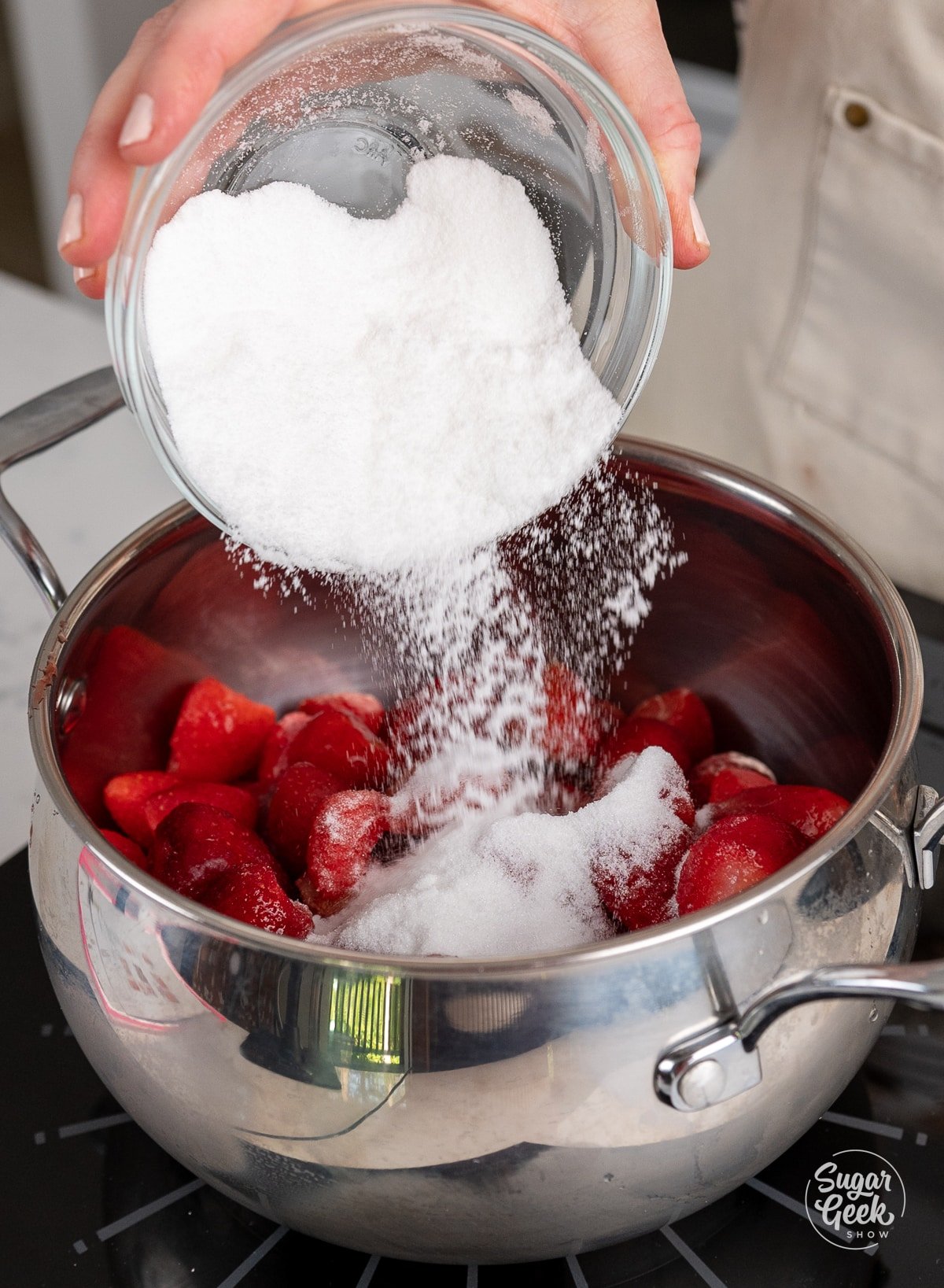 hand adding sugar to a pot with strawberries. 