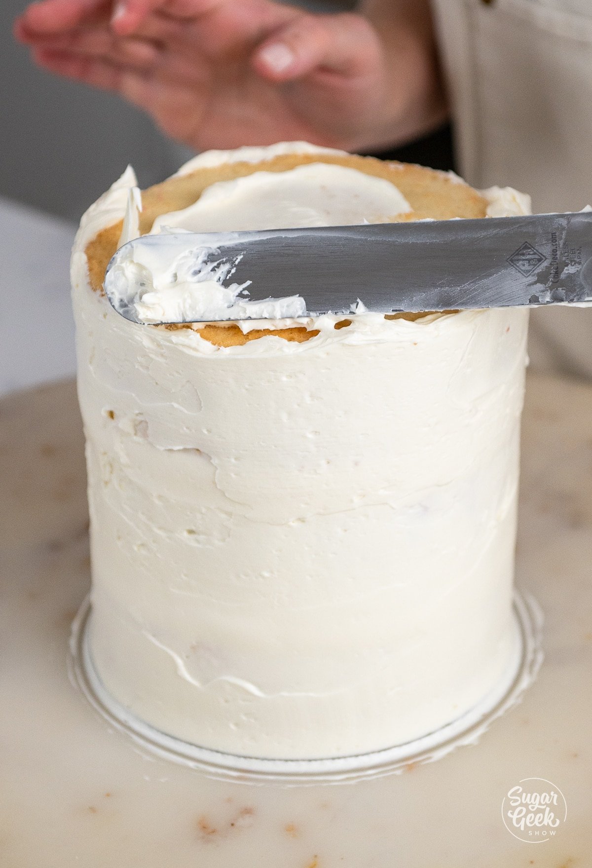 hands crumb coating the stacked cake with buttercream. 