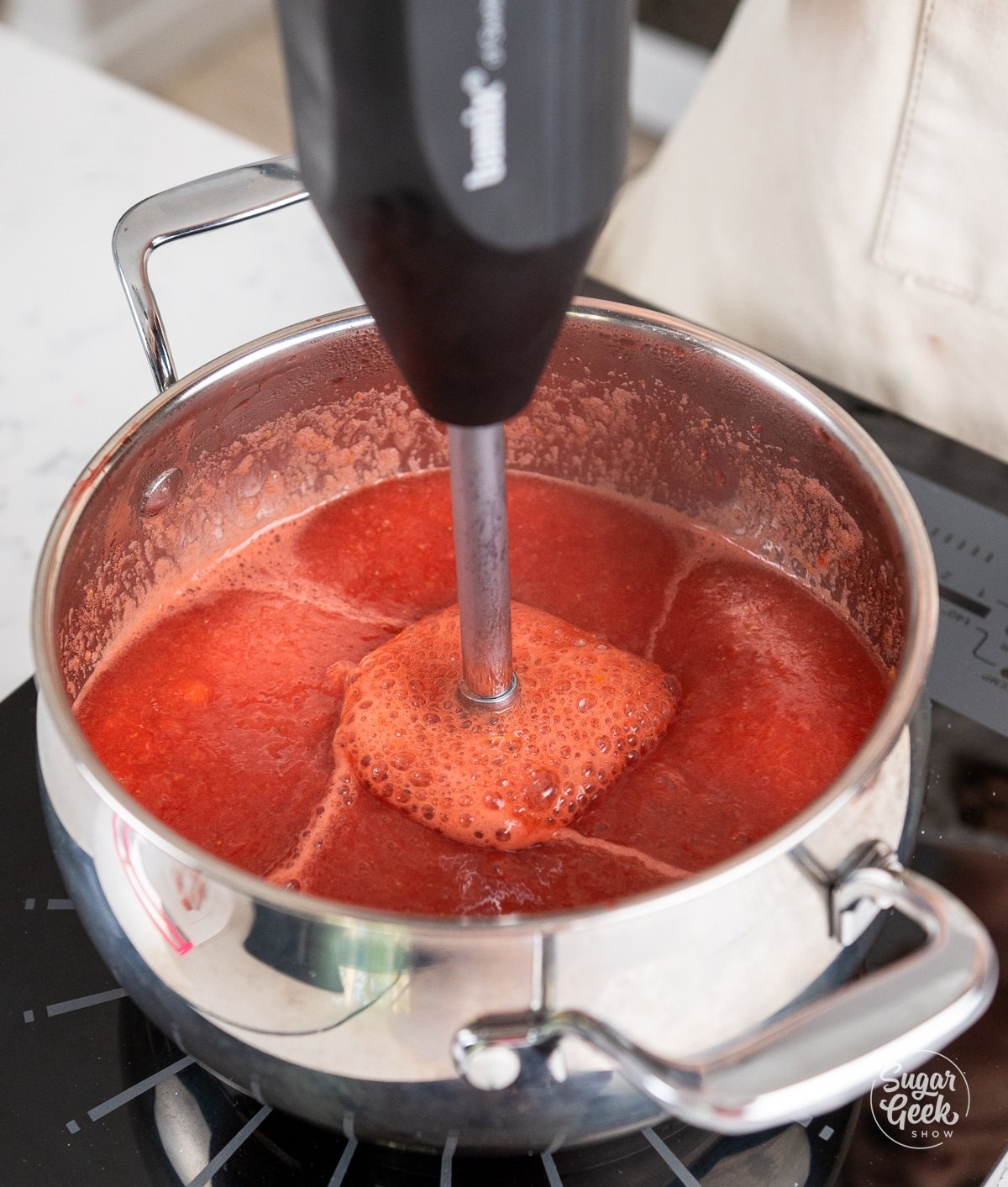Pot of cooked strawberries being blended with an immersion blender.
