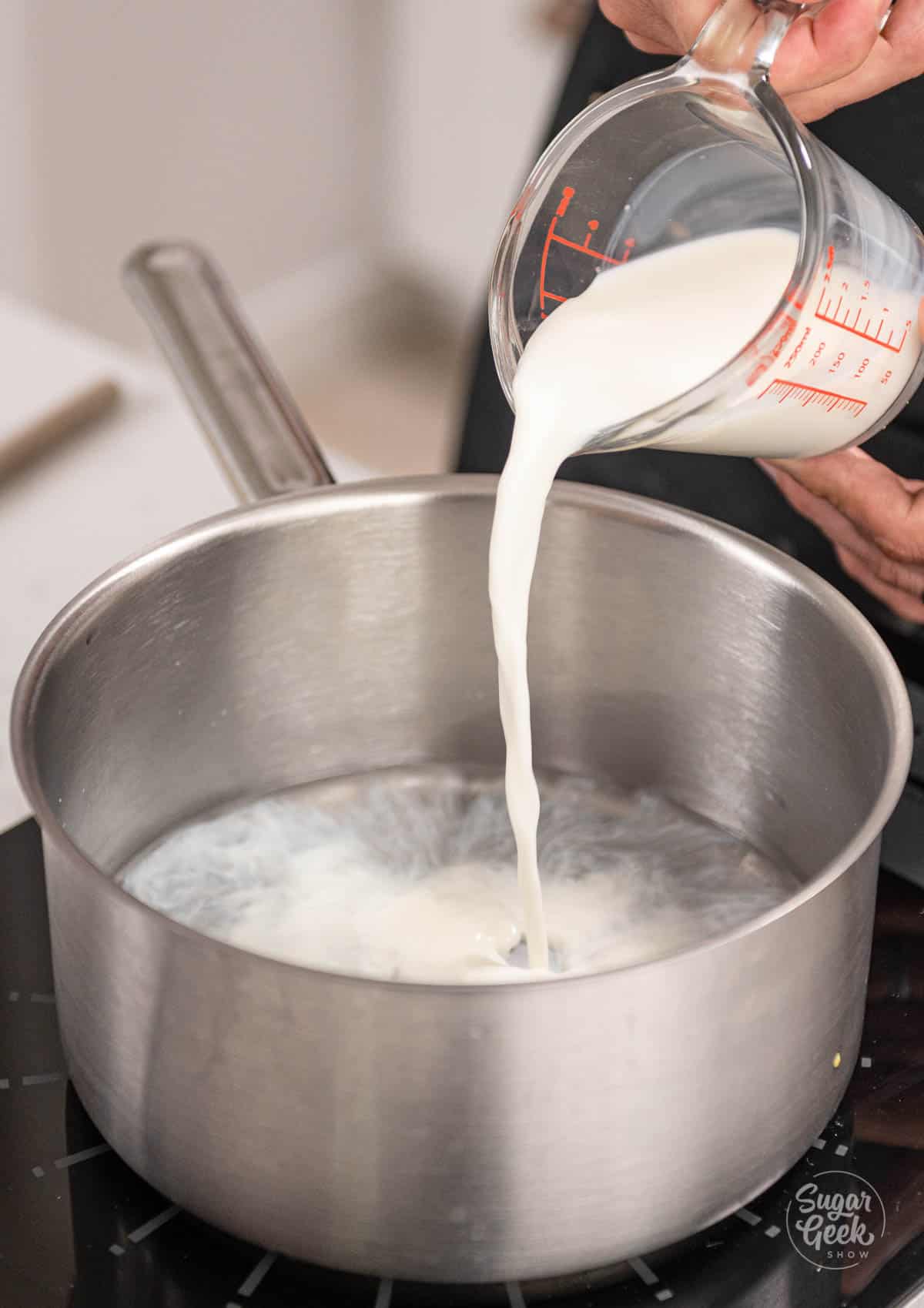 hand adding milk to a saucepan.