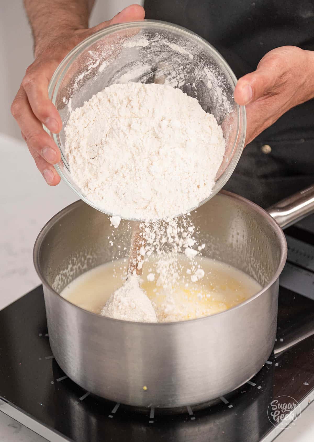 hands adding flour to saucepan.