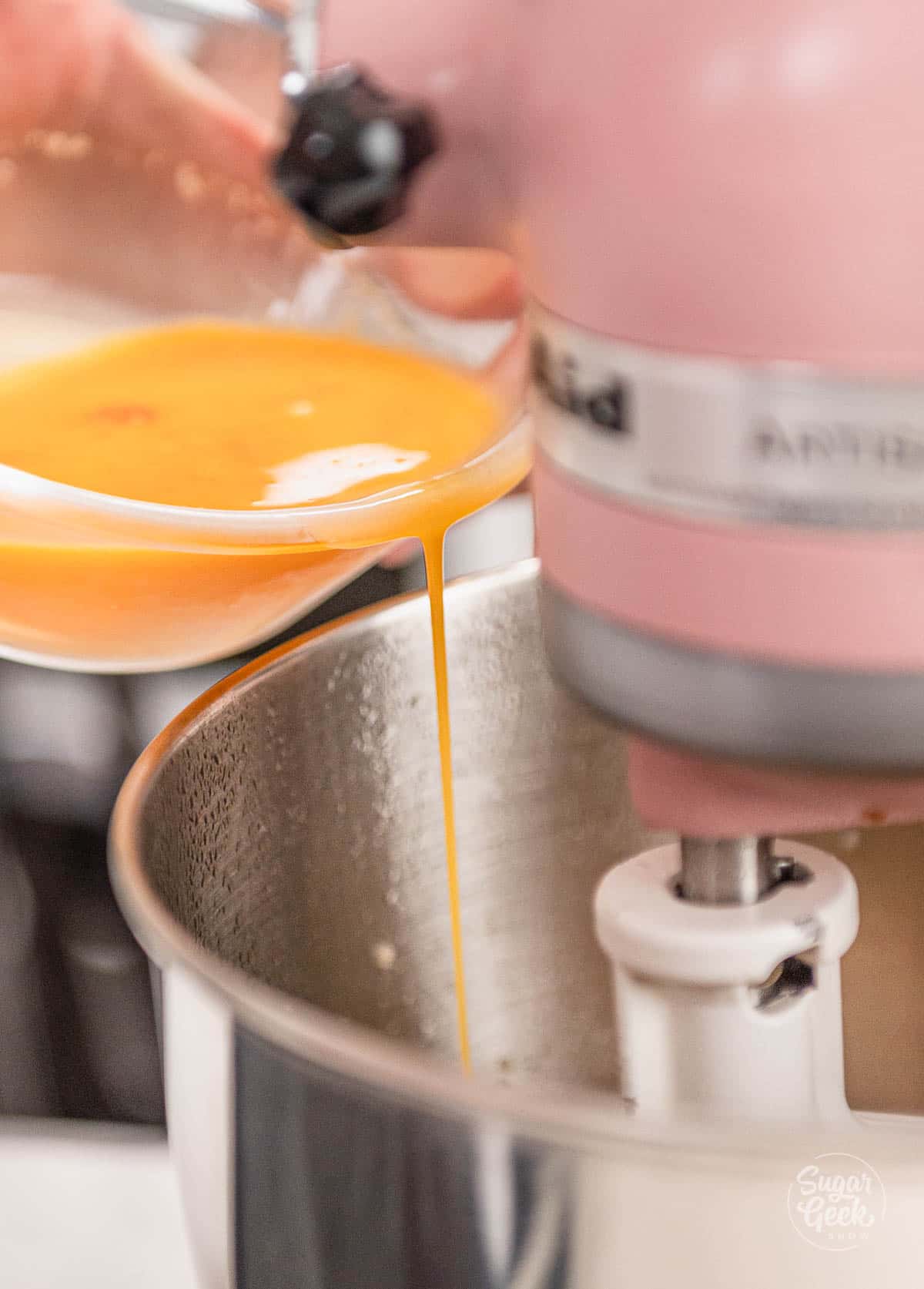 hand pouring eggs into stand mixer bowl.
