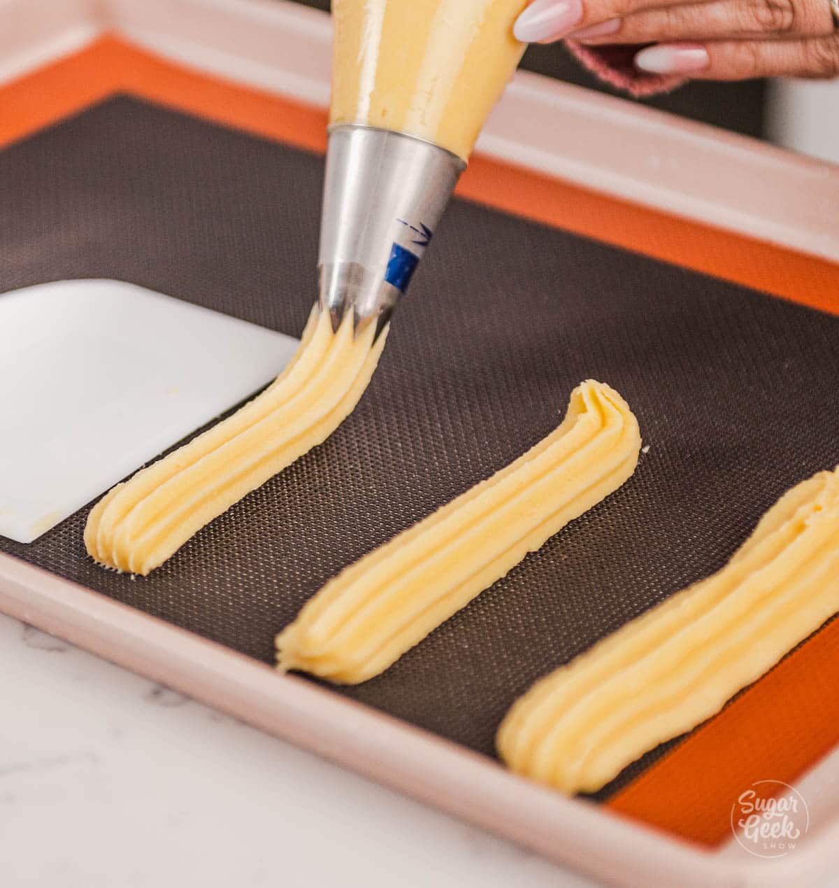 piping the choux dough into uniform lengths on a silpain mat.