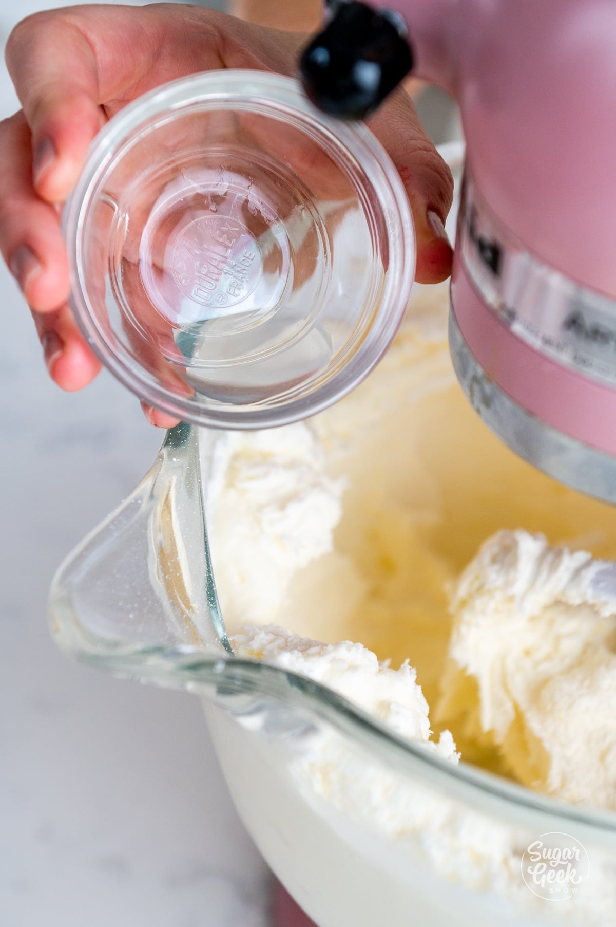 Hand adding clear vanilla to the stand mixer bowl.