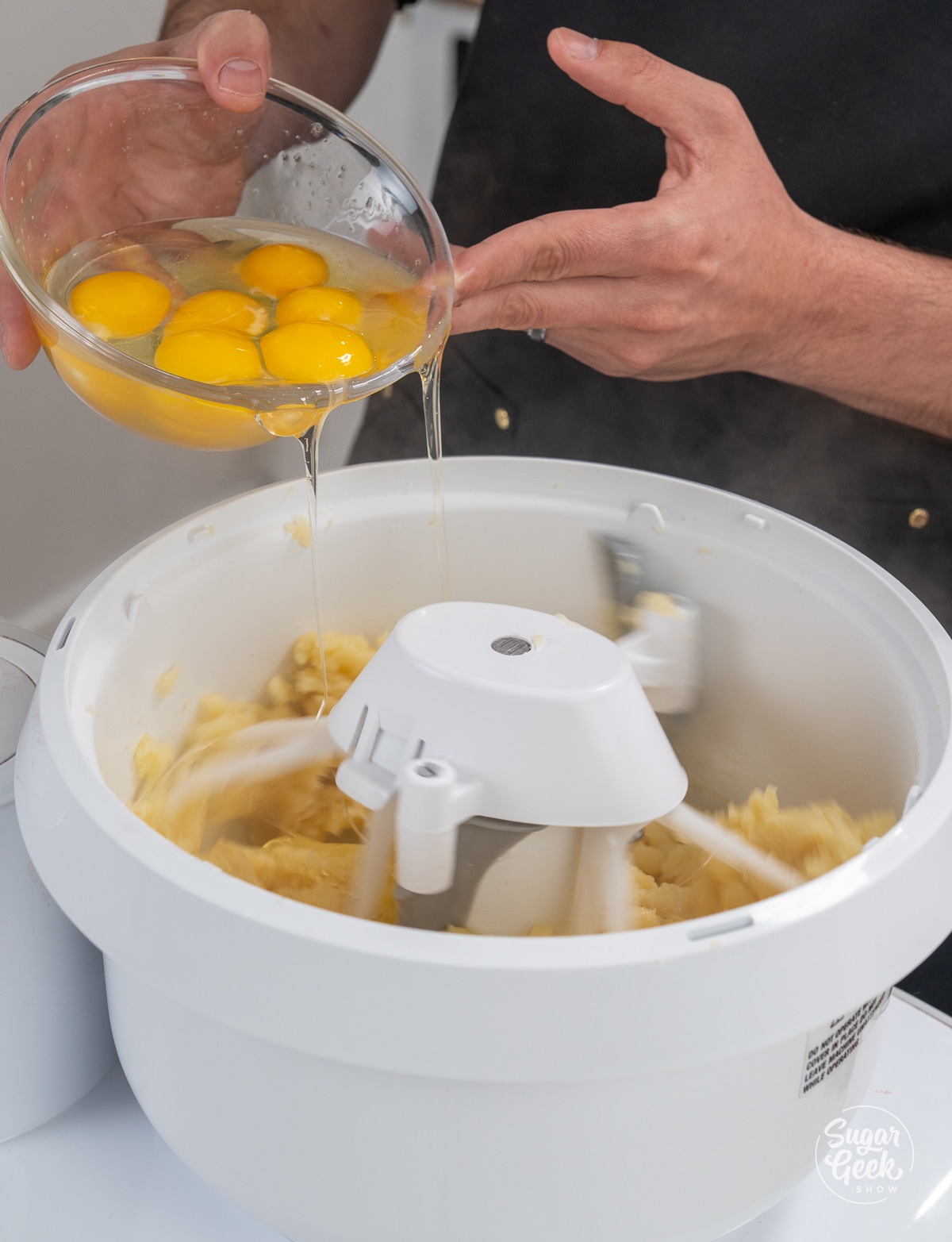 hands adding a bowl of eggs into a white stand mixer bowl