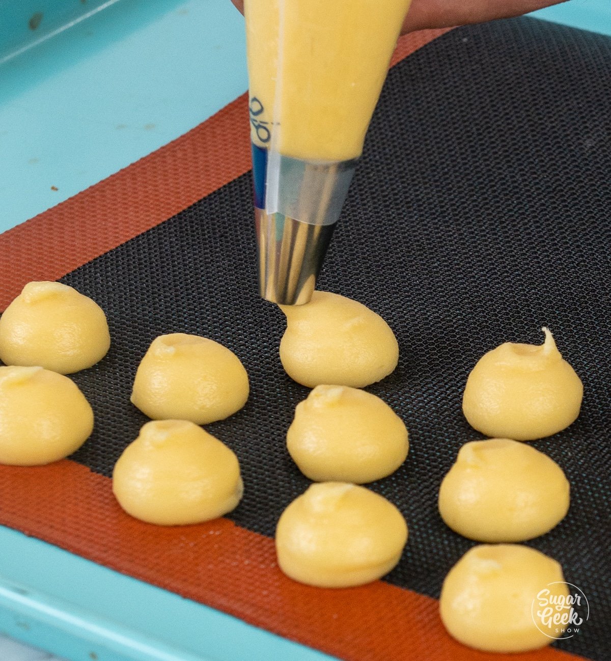 Piping choux dough into small round spheres on a baking sheet pan.